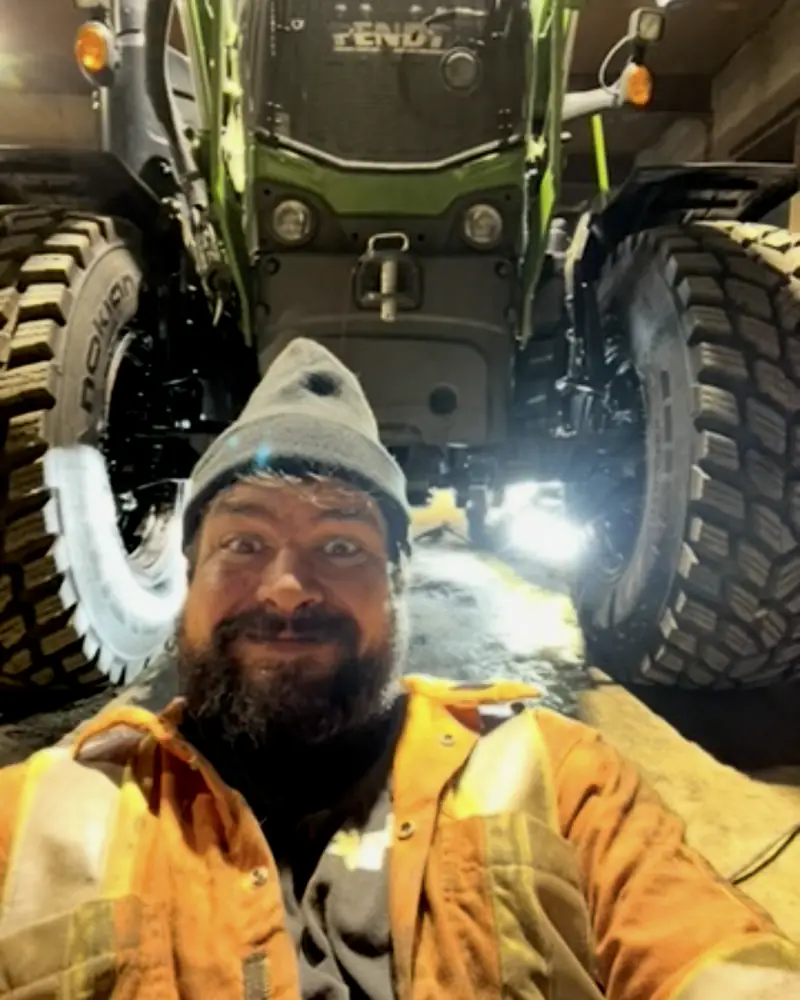 Simon Constantin, en tuque et manteau haute visibilité, devant son tracteur Fendt dans le garage de l'Entreprise SME