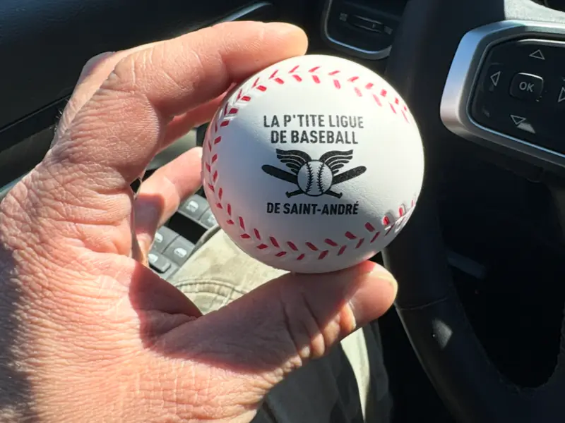 Balle de baseball tenue dans une main, portant l'inscription « La P'tite Ligue de baseball de Saint-André »