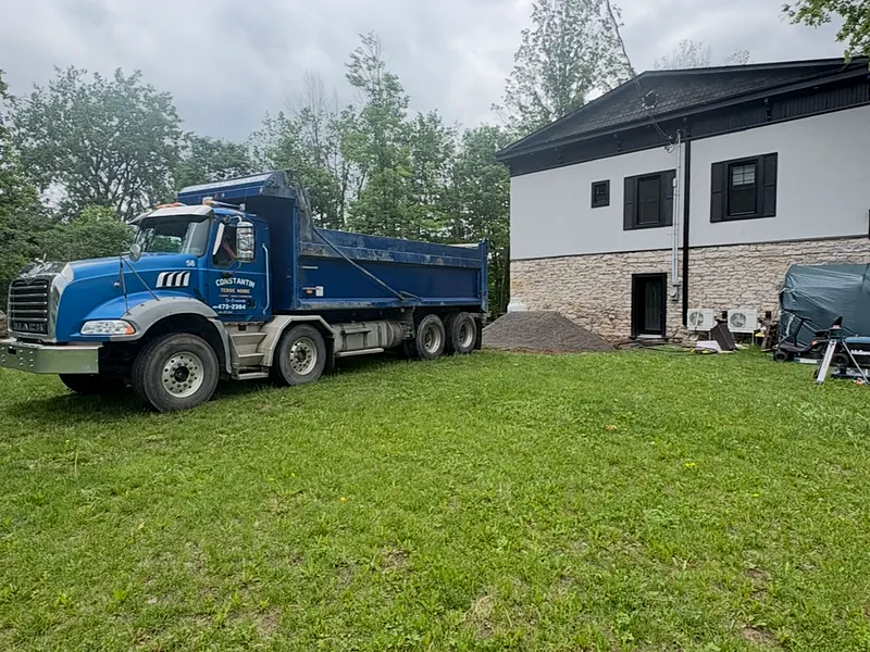 Camion douze roues bleu lettré Constantin Terre noire, tas de terre fraîchement livré à côté d'une maison
