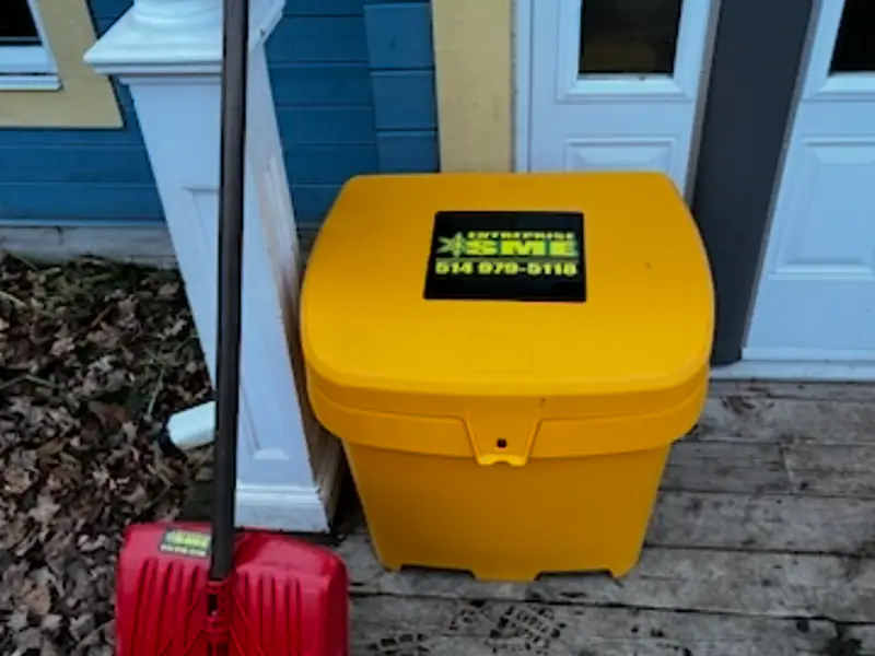 Bac à abrasif jaune estampillé Entreprise SME, posé près d'une entrée