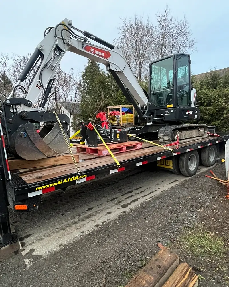 Mini-pelle Bobcat E42 sanglée et chaînée sur le fardier à col de cygne de l'Entreprise SME, prête pour le transport