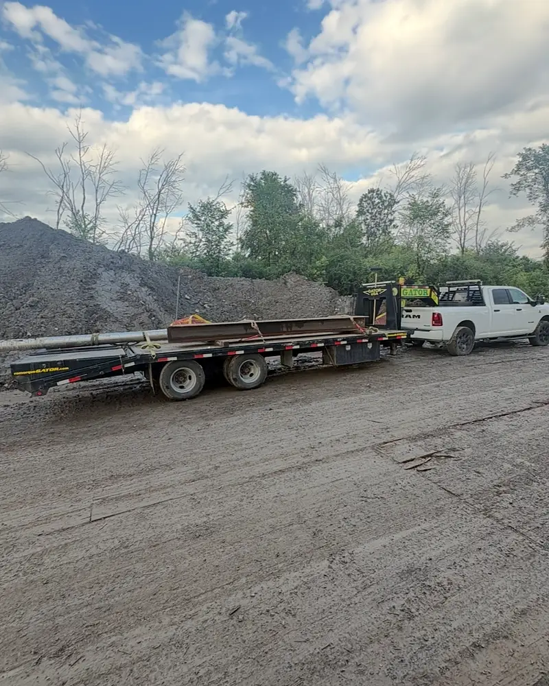 Fardier à col de cygne chargé de poutres et de tuyaux d'acier, attelé à la camionnette de l'Entreprise SME sur un chantier