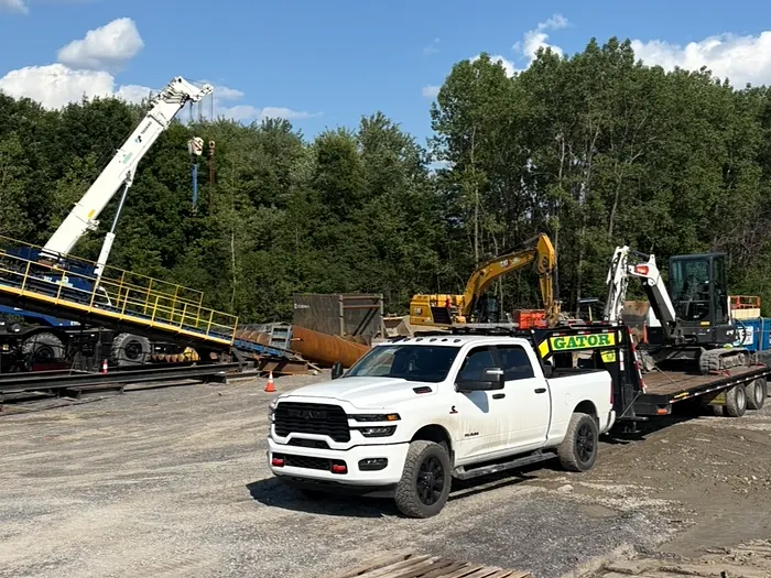 Camionnette de l'Entreprise SME et sa remorque chargée d'une pelle compacte, sur un chantier de construction