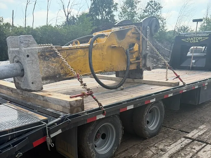 Marteau hydraulique jaune et son contrepoids de béton, chaînés sur le plateau de la remorque
