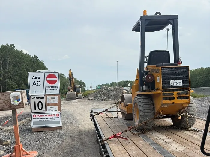Rouleau compacteur jaune enchaîné sur la remorque, à l'entrée d'un chantier routier