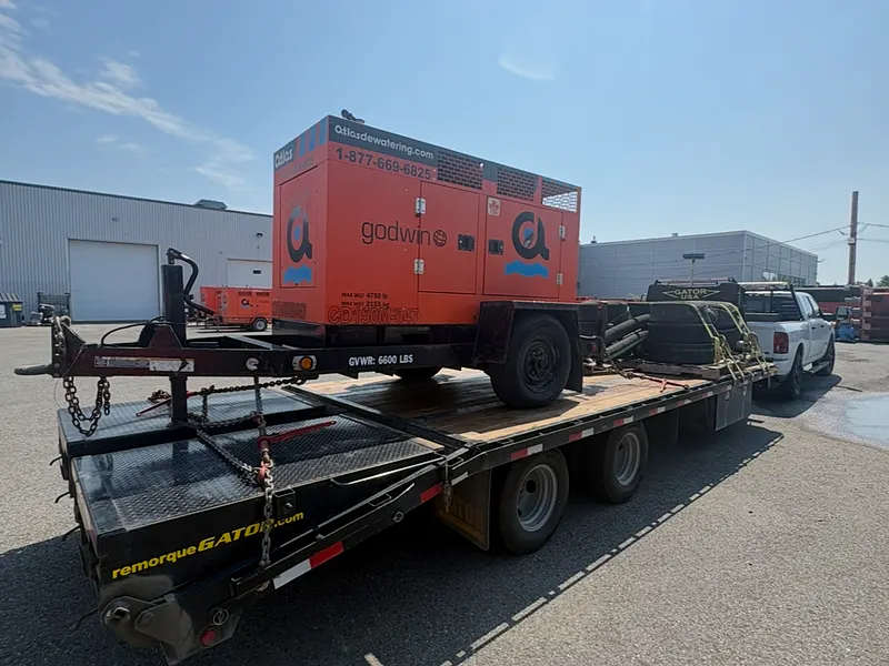 Pompe industrielle orange chargée et sanglée sur le fardier à col de cygne de l'Entreprise SME