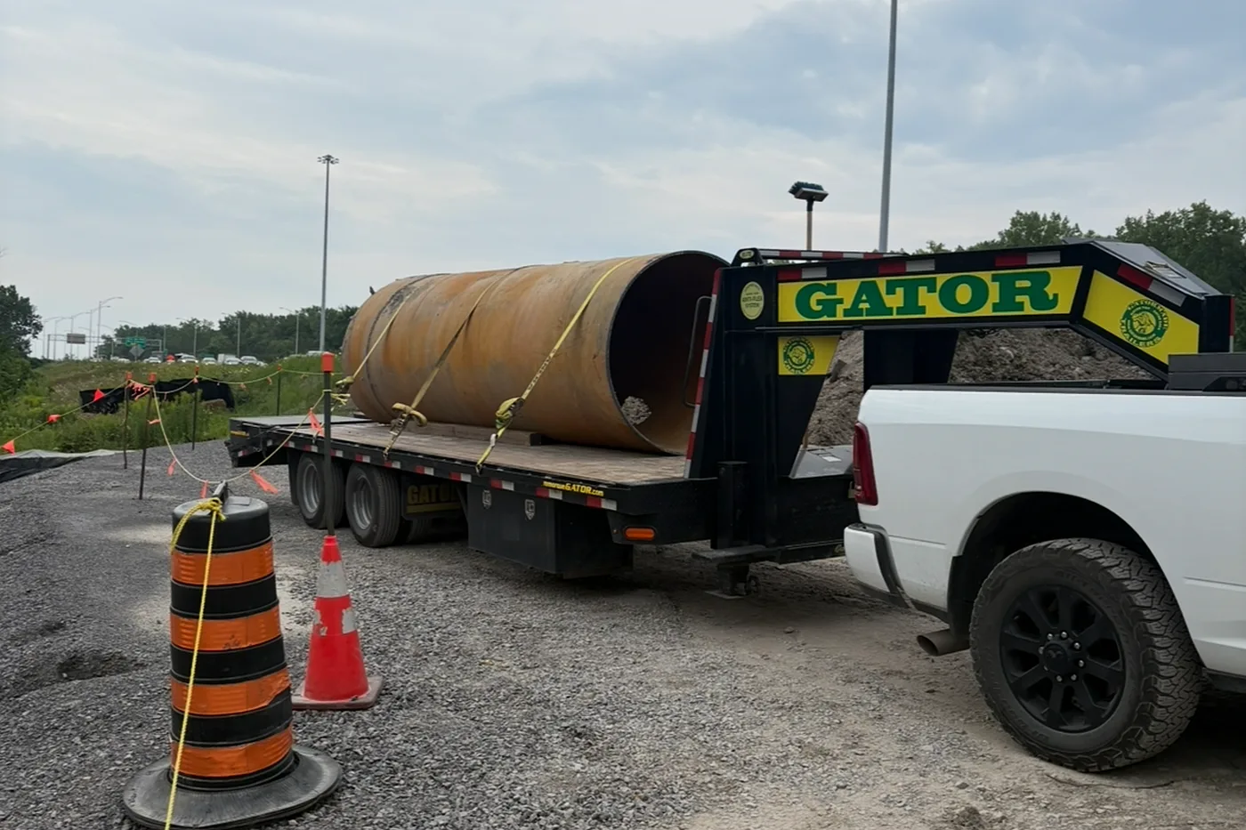 Remorque à col de cygne de l'Entreprise SME chargée d'une grosse conduite d'acier, attelée à la camionnette sur un chantier routier